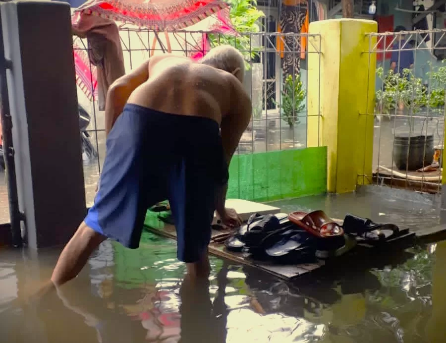 Salah satu warga mengamankan sendal milik keluarganya agar tidak terbawa arus banjir. (Ist)